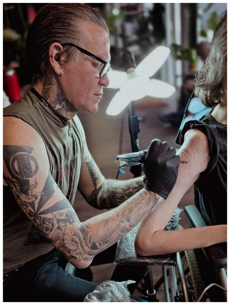 Ein Kunde im Rollstuhl lässt sich im Autark Tattoo Studio Berlin Charlottenburg tätowieren. Durch flexible Arbeitsplätze können Tätowierer auch Menschen mit körperlichen Einschränkungen professionell tätowieren.